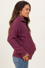 woman wearing a burgundy maternity sweater with a half zip, showcasing her baby bump from the side