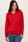 woman wearing a red half-zip sweater with a textured knit and long sleeves paired with blue jeans