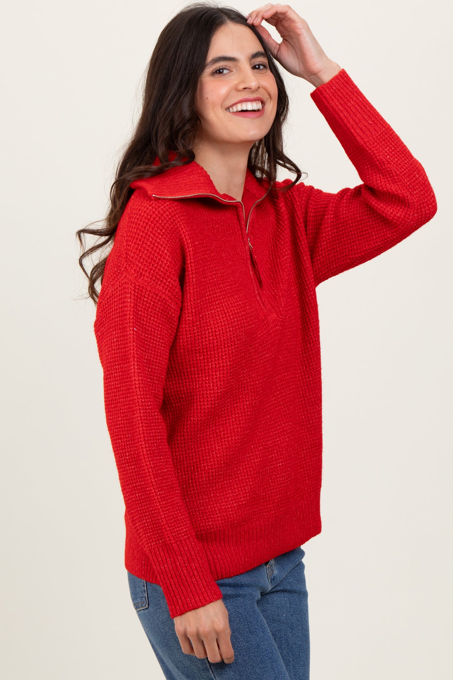 woman wearing a bright red half-zip textured sweater and smiling against a light background