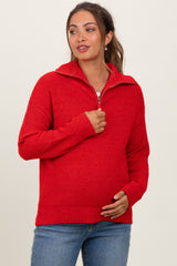 woman wearing a red maternity zip-up sweater and holding her baby bump with a casual outfit