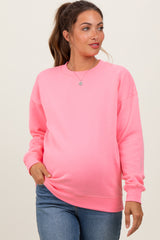 woman wearing a bright pink maternity sweatshirt and showing her baby bump while smiling