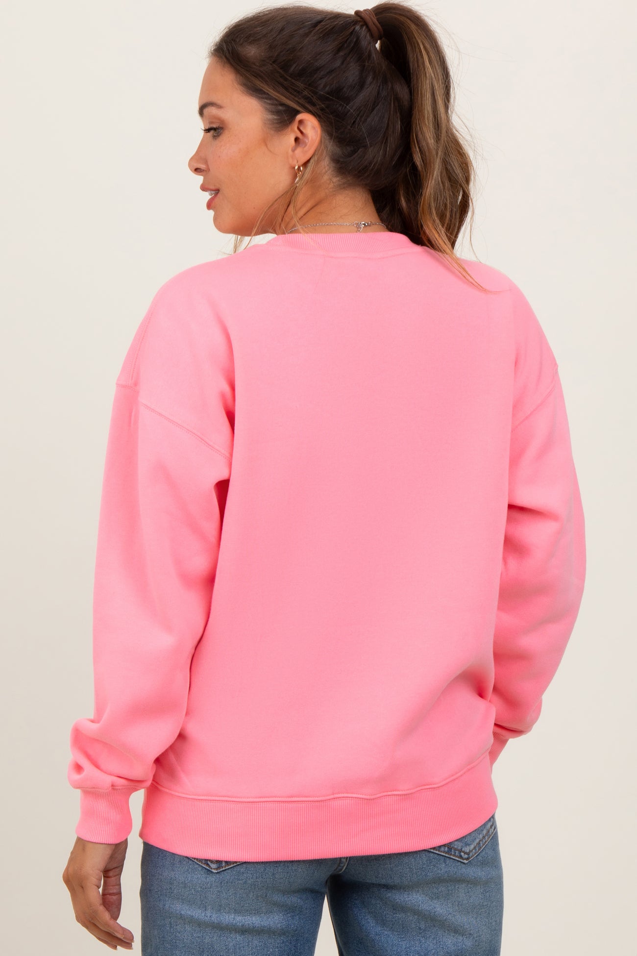 woman wearing a bright pink maternity sweatshirt with a relaxed fit and long sleeves, showing her back