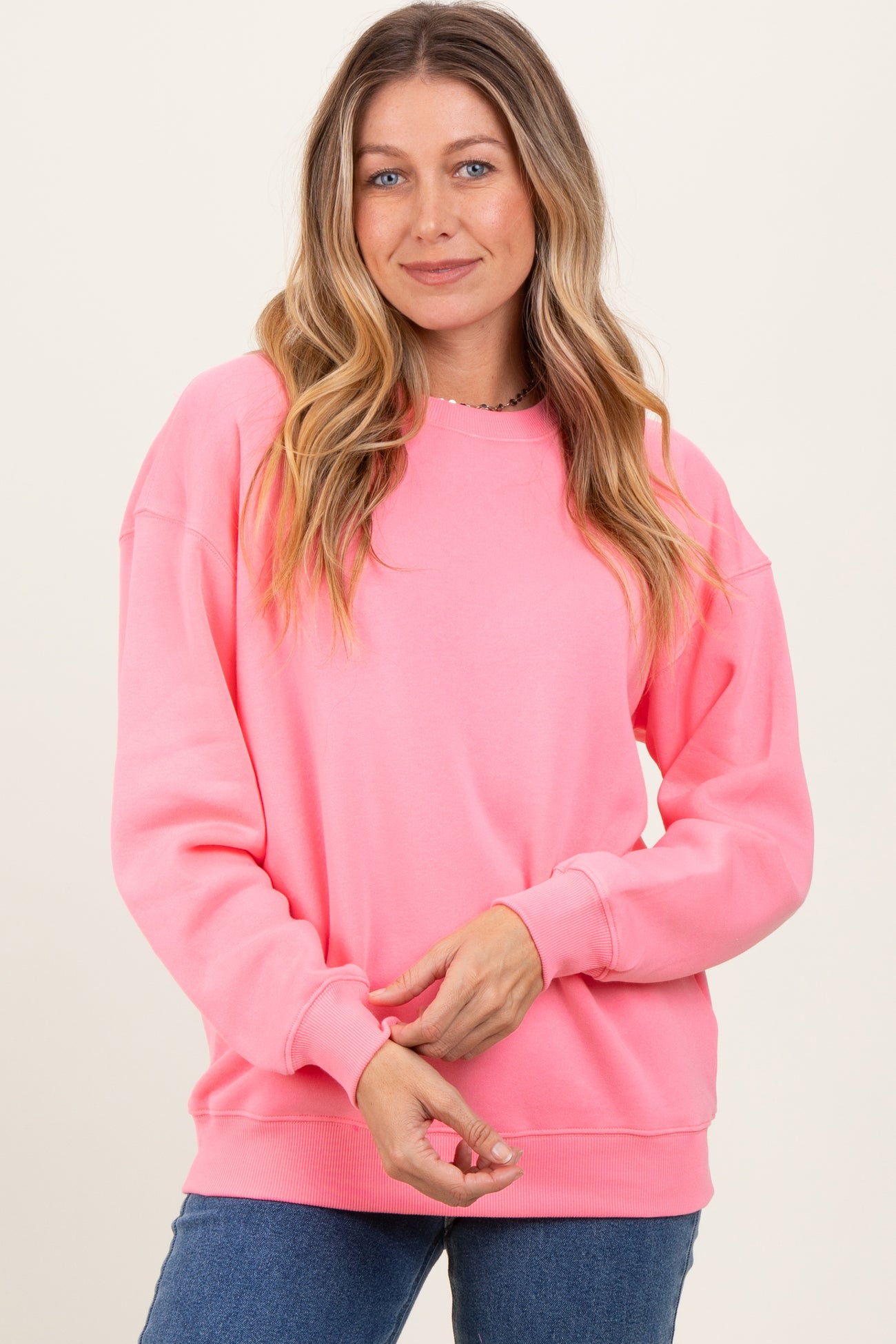 woman wearing a bright pink long sleeve oversized sweatshirt and smiling