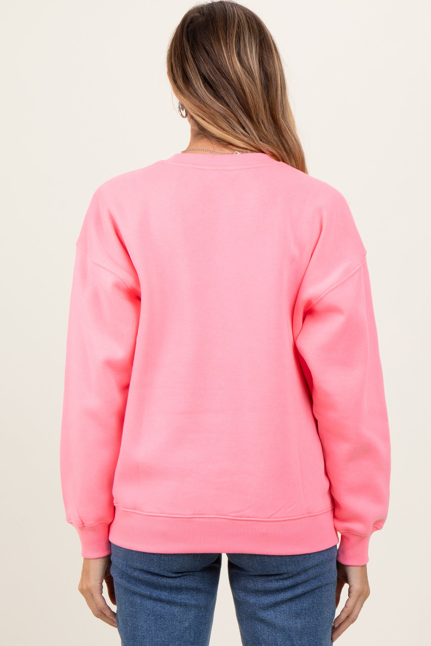 woman wearing a bright pink oversized sweatshirt, showcasing a relaxed fit and ribbed cuffs, viewed from the back
