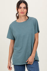 woman wearing a teal short sleeve t-shirt and blue jeans standing confidently against a neutral background
