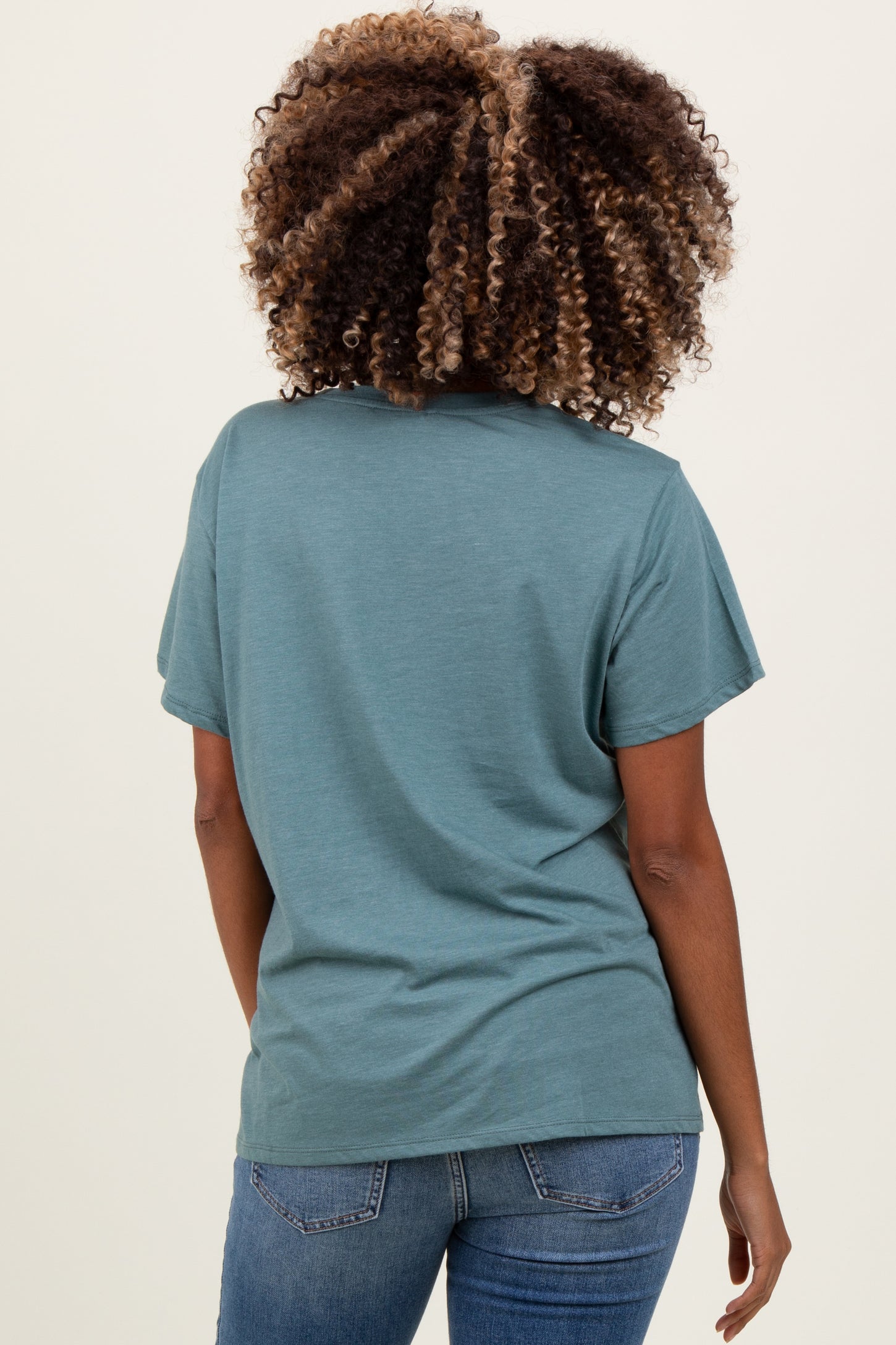 woman wearing a teal short sleeve maternity top and blue jeans, showing her back and curly hair