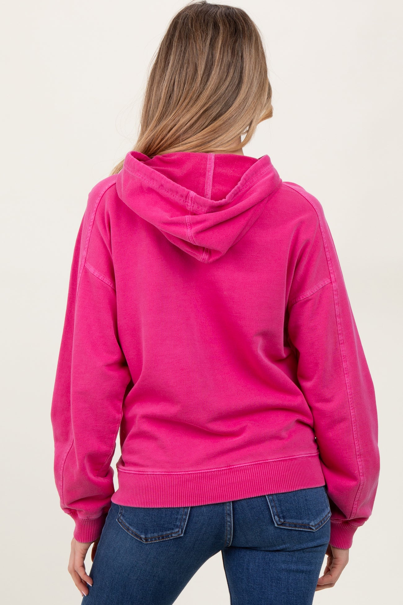 woman wearing a bright pink maternity hoodie, shown from the back, paired with blue jeans