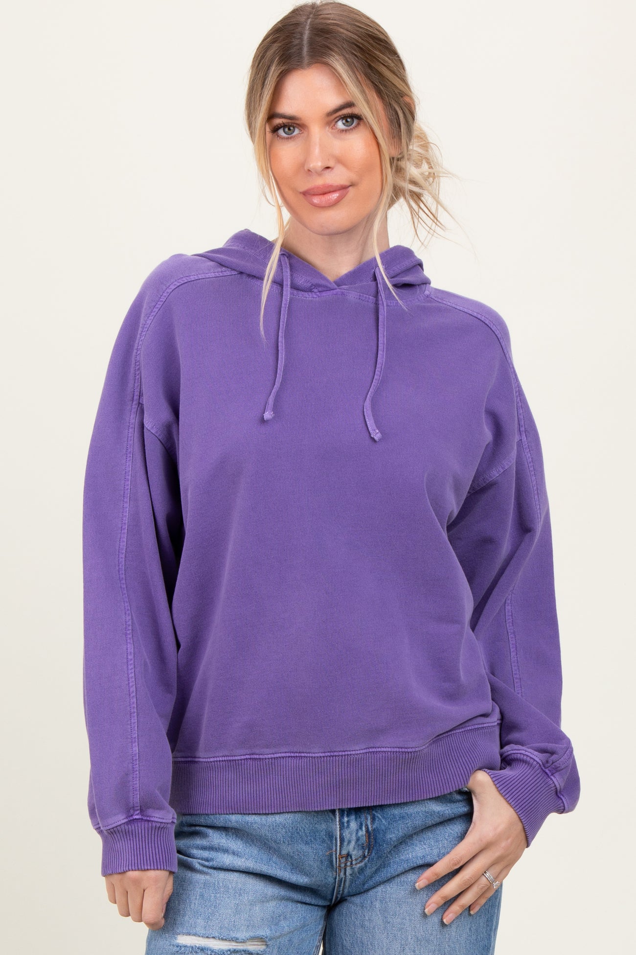 woman wearing a purple oversized hoodie with a drawstring and relaxed fit, paired with light blue jeans