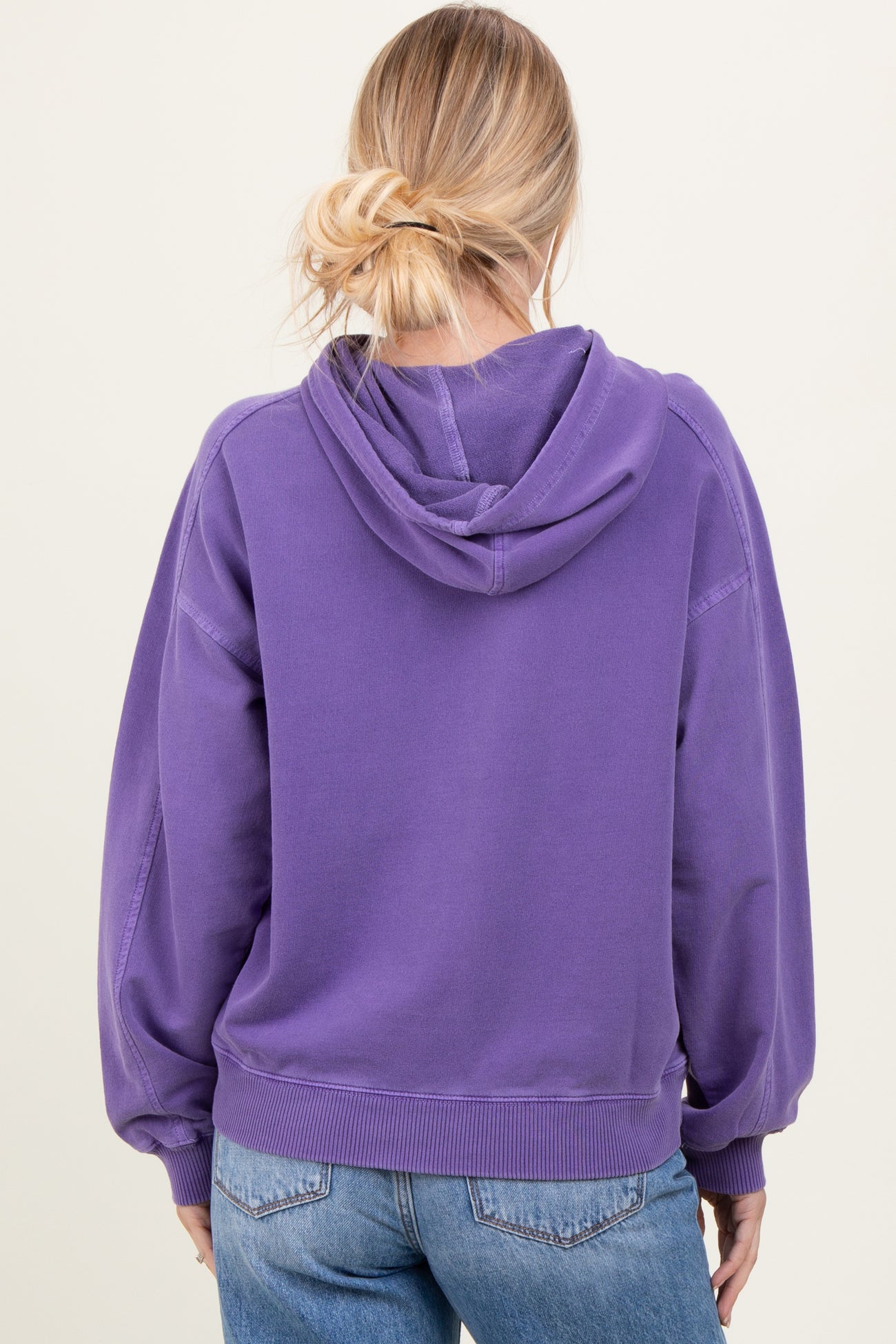 woman wearing a purple oversized hoodie with a back view and kangaroo pocket, paired with light blue jeans