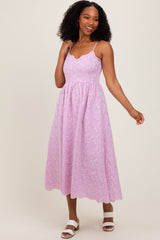 woman wearing a lilac midi dress with a scalloped neckline and floral details, styled with white sandals