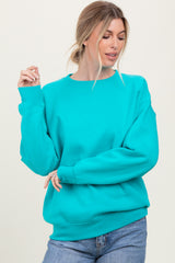 woman wearing a turquoise oversized sweatshirt and light blue jeans, smiling with a playful pose