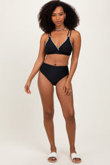 woman wearing a black bikini with embellished detailing and high-waisted bottoms, standing confidently