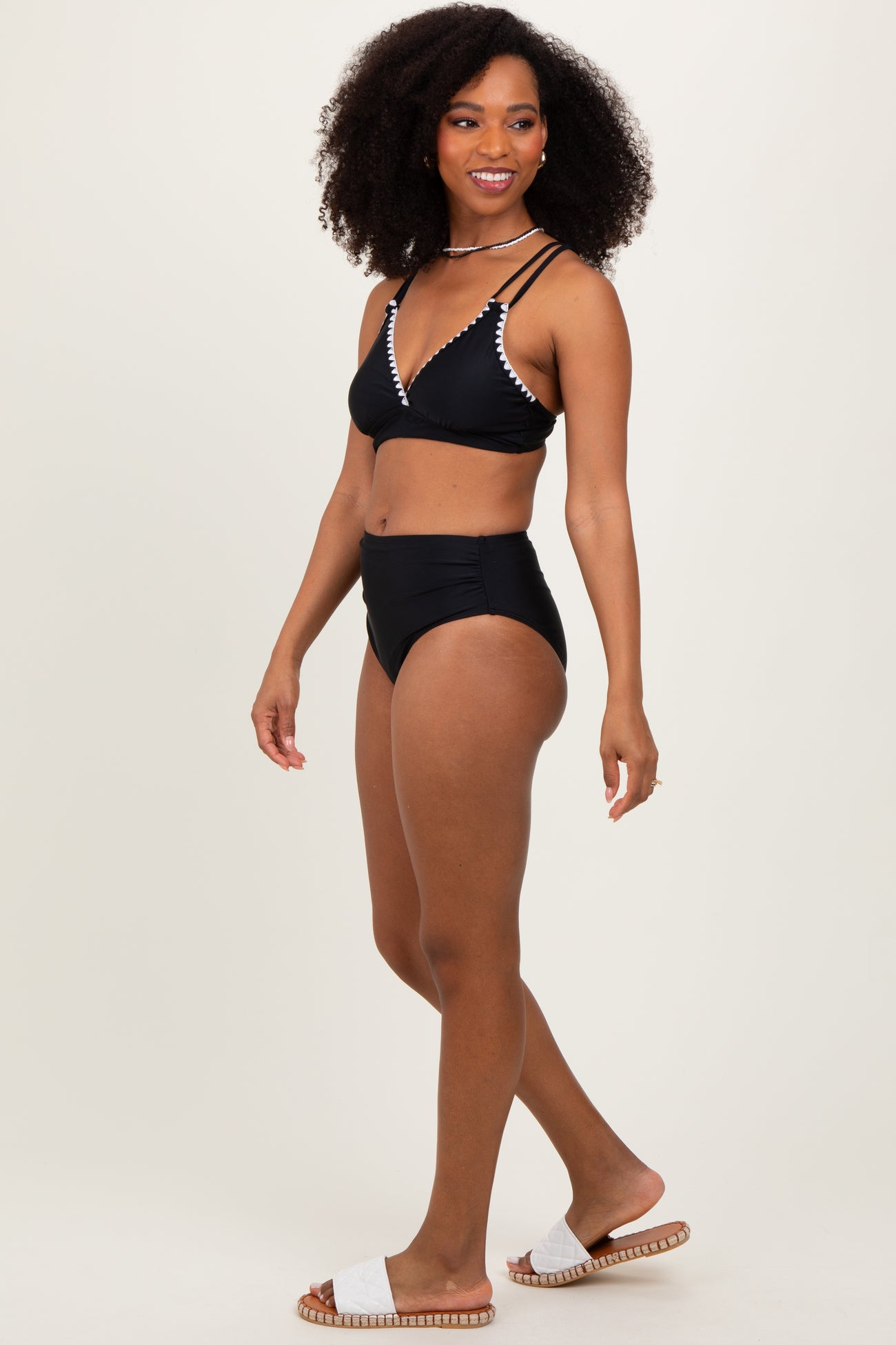 woman wearing a black bikini with beaded detail and high-waisted bottoms, standing on a neutral background