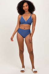 woman wearing a blue bikini with white detailing and high-waisted bottoms, standing with a light smile