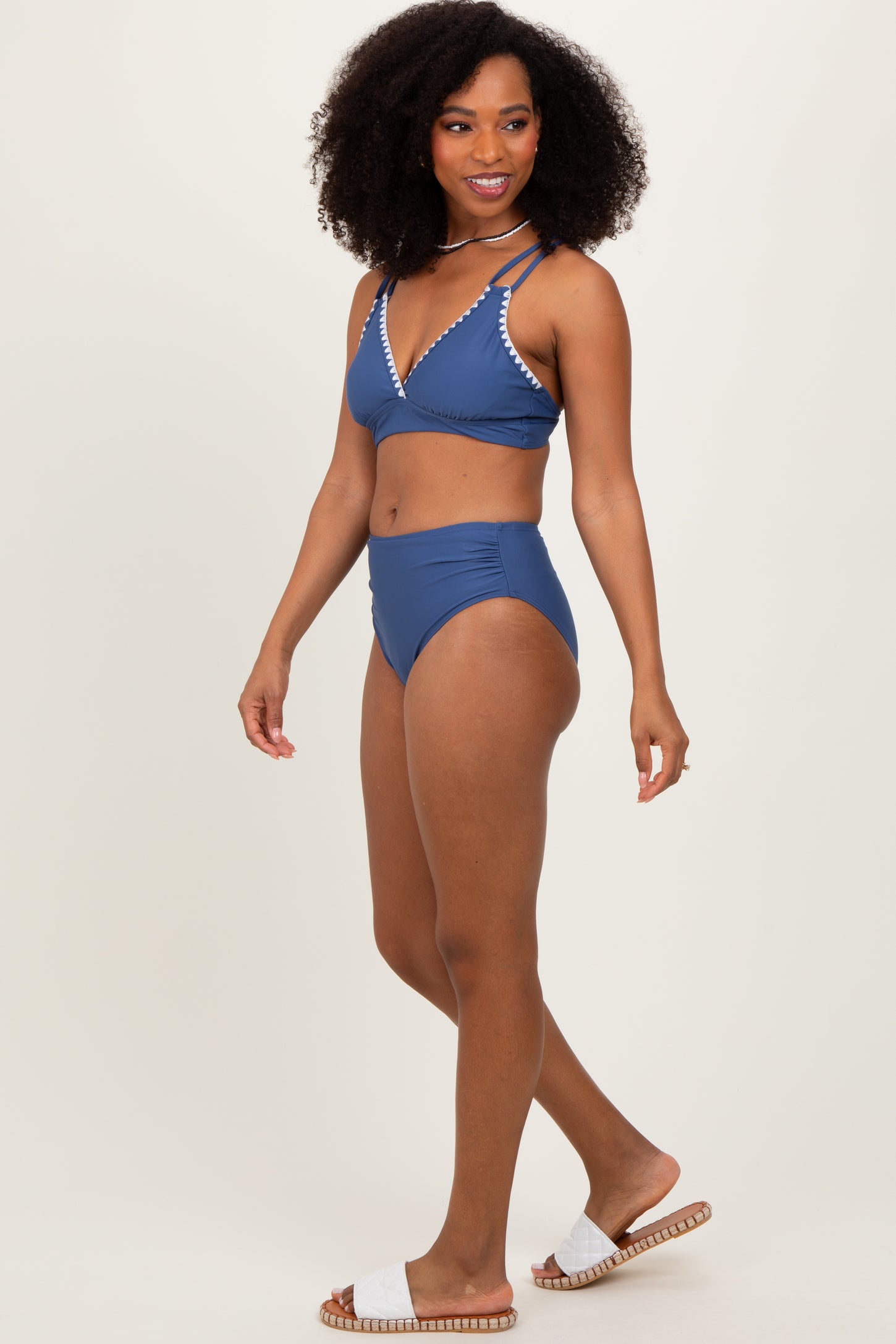 woman wearing a navy blue bikini with a triangular top and high-waisted bottom, styled with white detailing and sandals