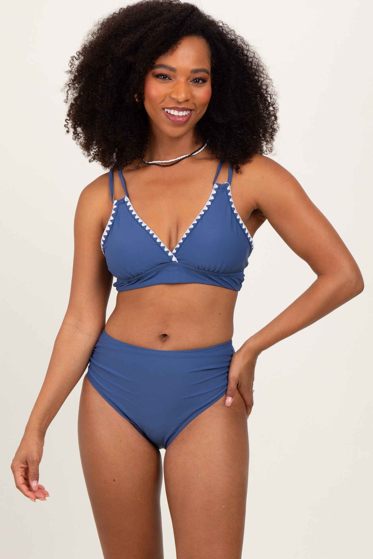 woman wearing a blue bikini with white trim and high-waisted bottoms, smiling at the camera