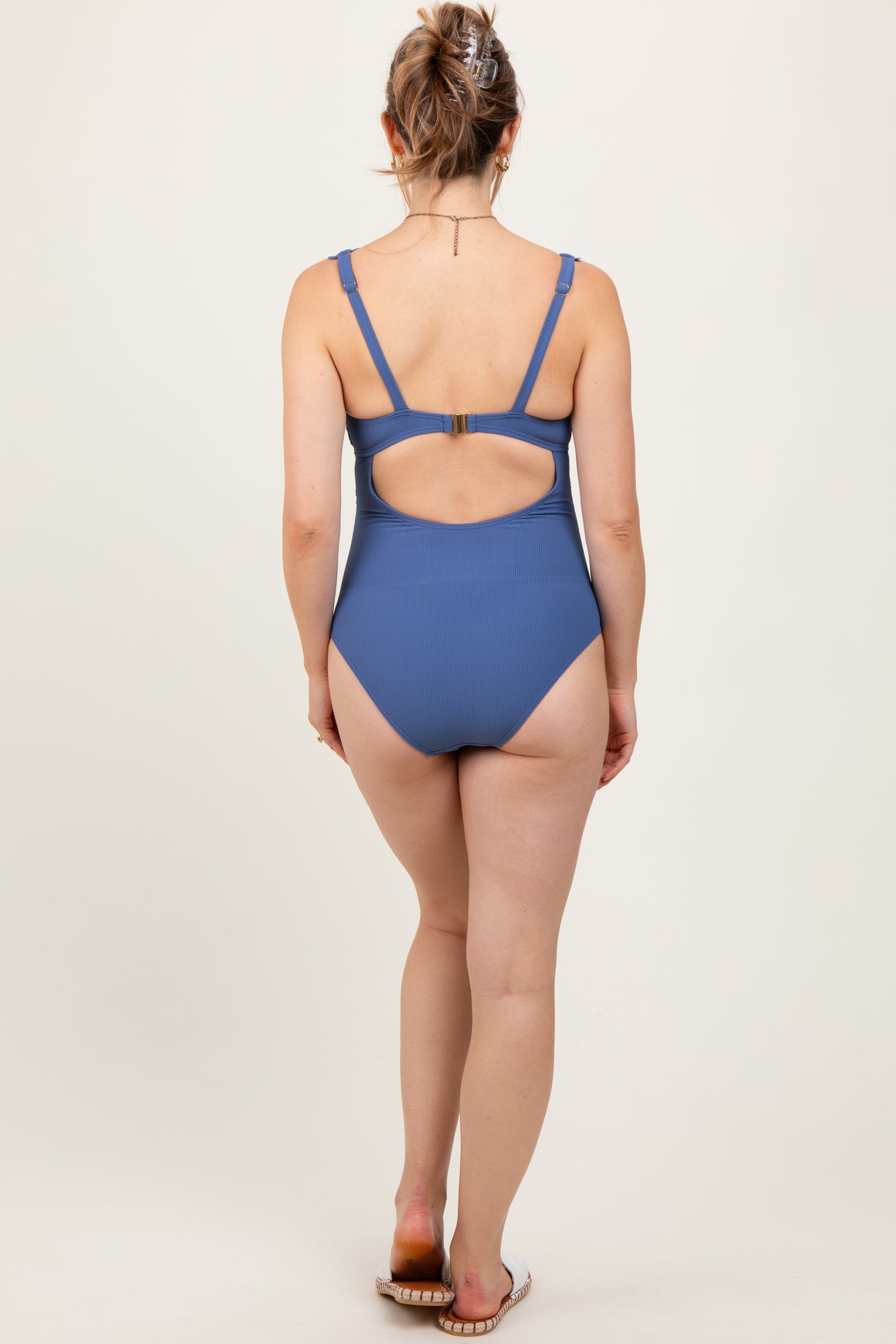 woman wearing a blue ribbed maternity swimsuit with a cutout back design, showing no visible baby bump