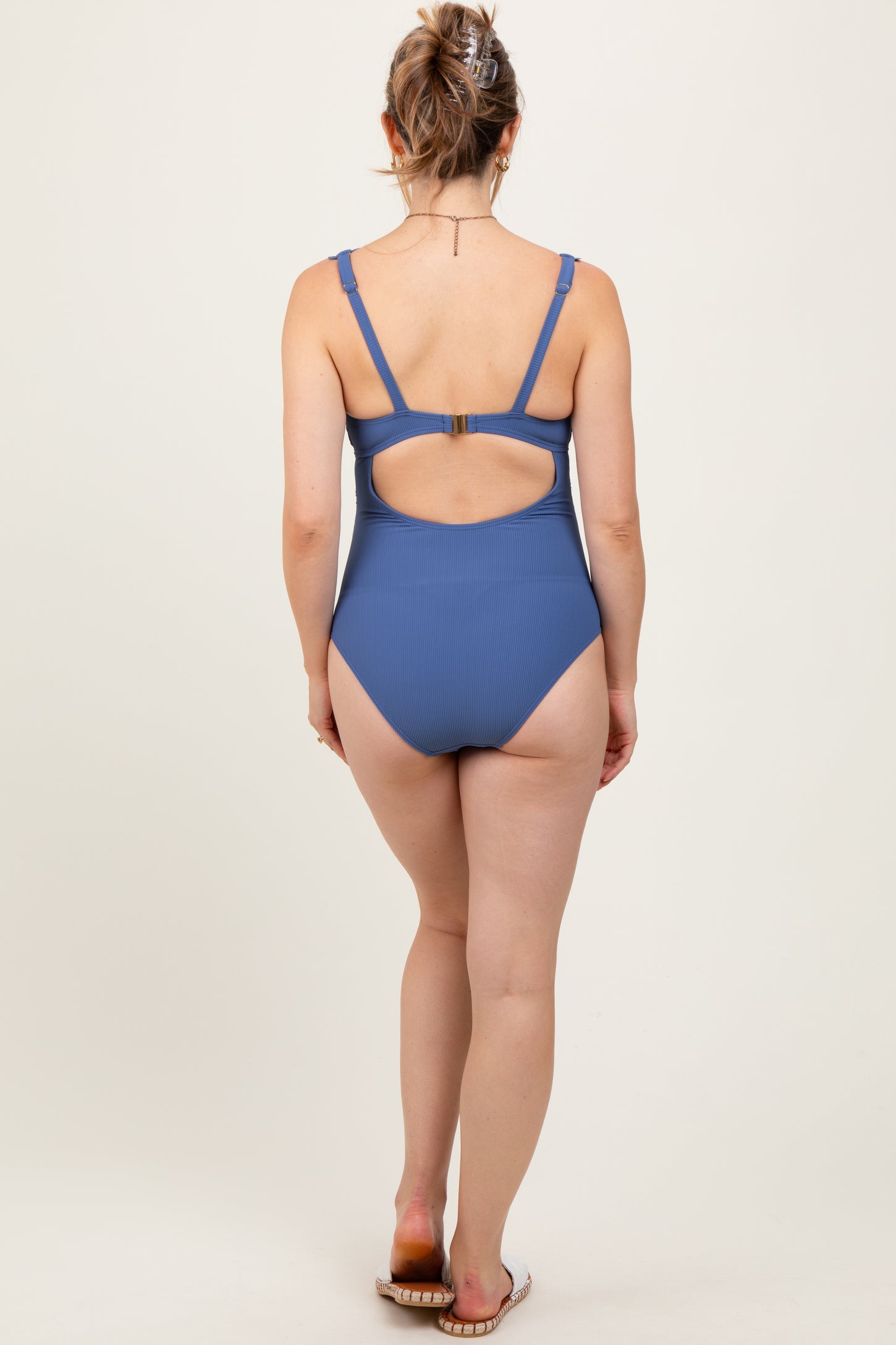 woman wearing a blue ribbed maternity swimsuit with a cutout back design, showing no visible baby bump
