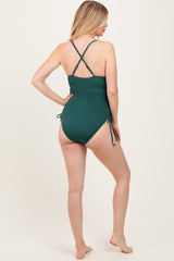 woman wearing a dark green maternity one-piece swimsuit with adjustable side ties and crisscross back straps