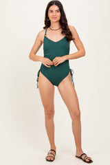 woman wearing a dark green ribbed one-piece swimsuit with adjustable straps and side ties