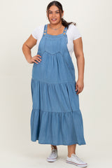 woman wearing a light blue denim maxi dress with adjustable straps and tiered skirt style