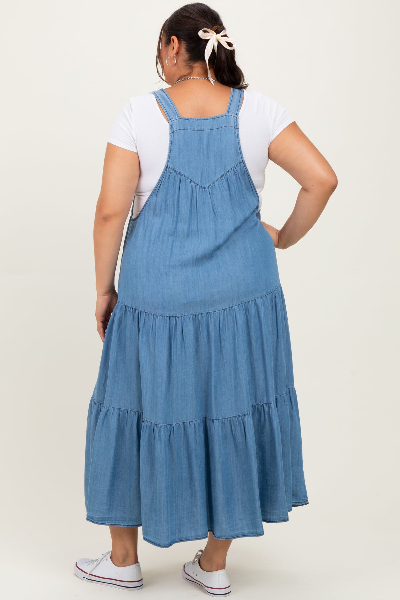 woman wearing a light blue denim maxi dress with tiered ruffles and adjustable straps, seen from the back