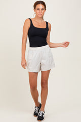 woman wearing a black sleeveless bodysuit and light gray athletic shorts, standing with one hand on her hip