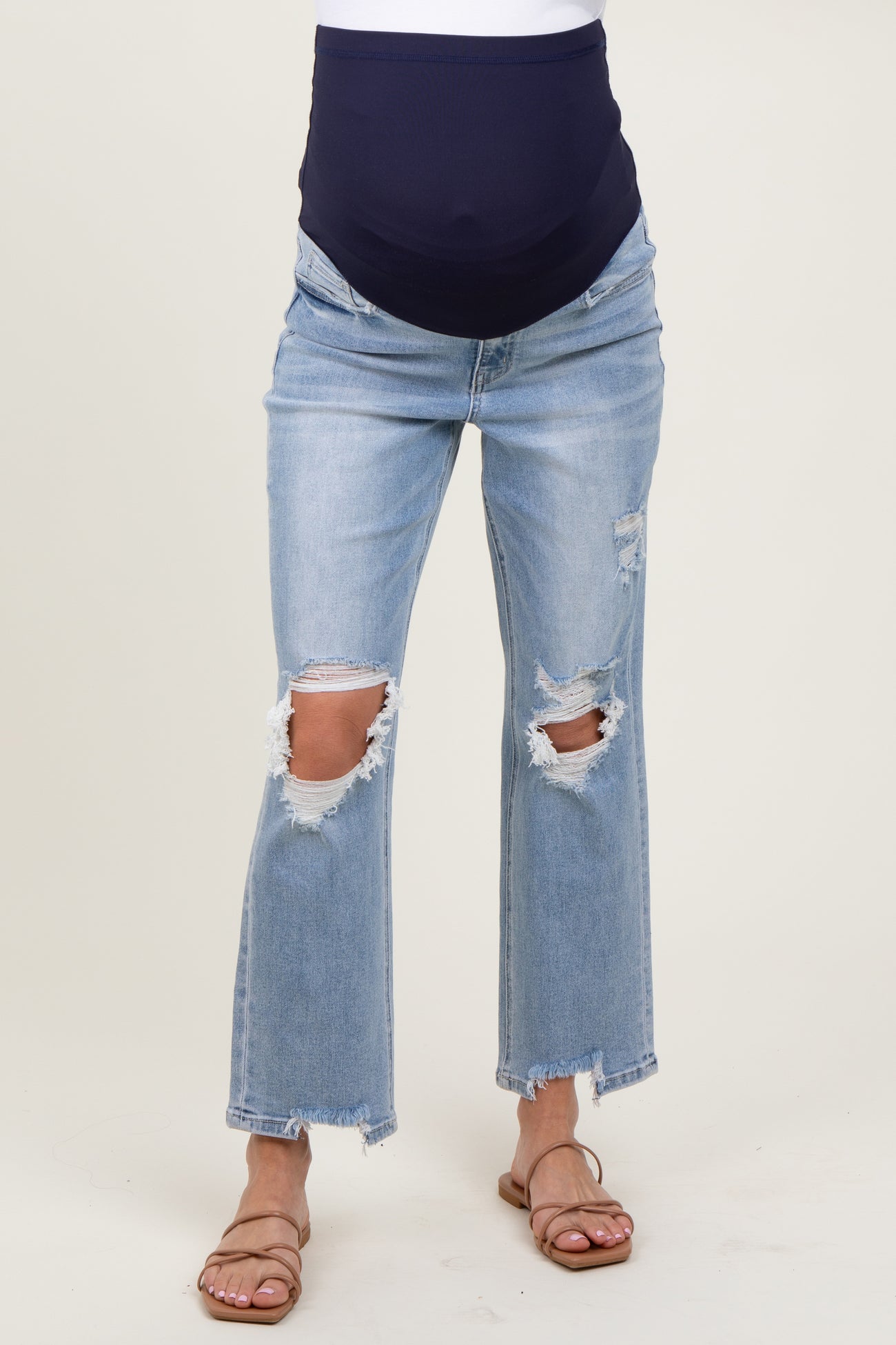 woman wearing distressed light blue maternity jeans with a dark blue over-the-bump panel and open-toe sandals
