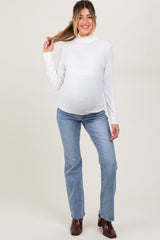 woman wearing a white long sleeve maternity top and blue jeans, showing her baby bump while posing with her hair