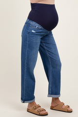 woman wearing a pair of distressed blue maternity jeans with a dark blue over-the-bump band and brown sandals, showing her baby bump
