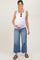 woman wearing a white maternity tank top and distressed wide-leg jeans, smiling and holding her baby bump