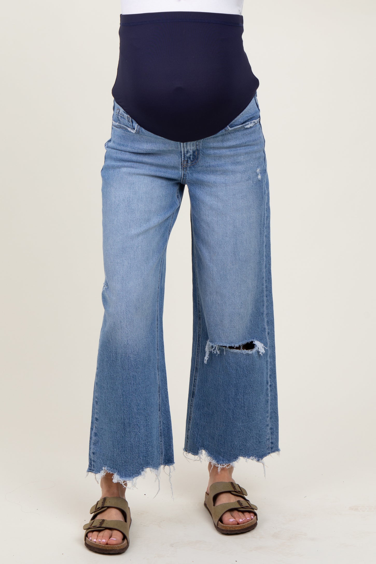 woman wearing a navy blue maternity top with a baby bump and distressed wide-leg denim jeans