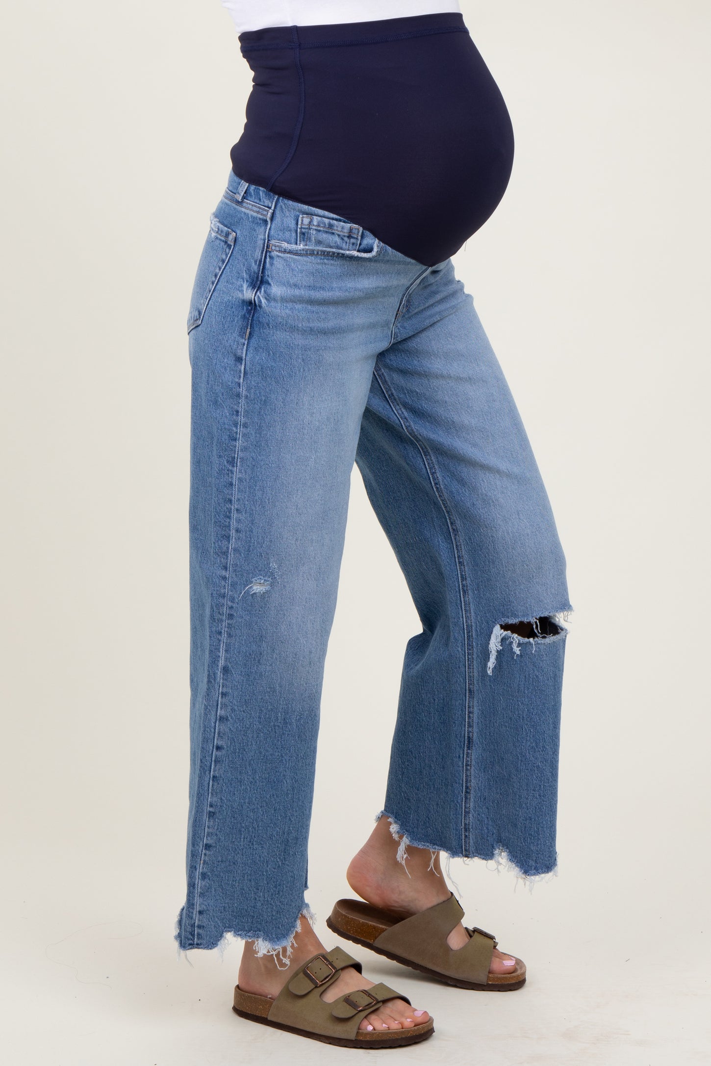 woman wearing light blue distressed maternity jeans with a navy blue over-the-bump panel and revealing her baby bump