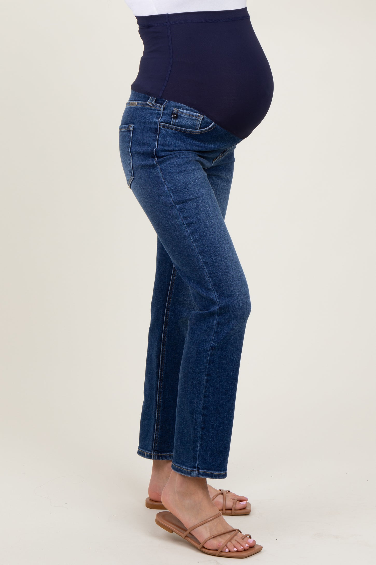 woman wearing a navy blue maternity belly band with dark wash straight leg jeans and showing her baby bump