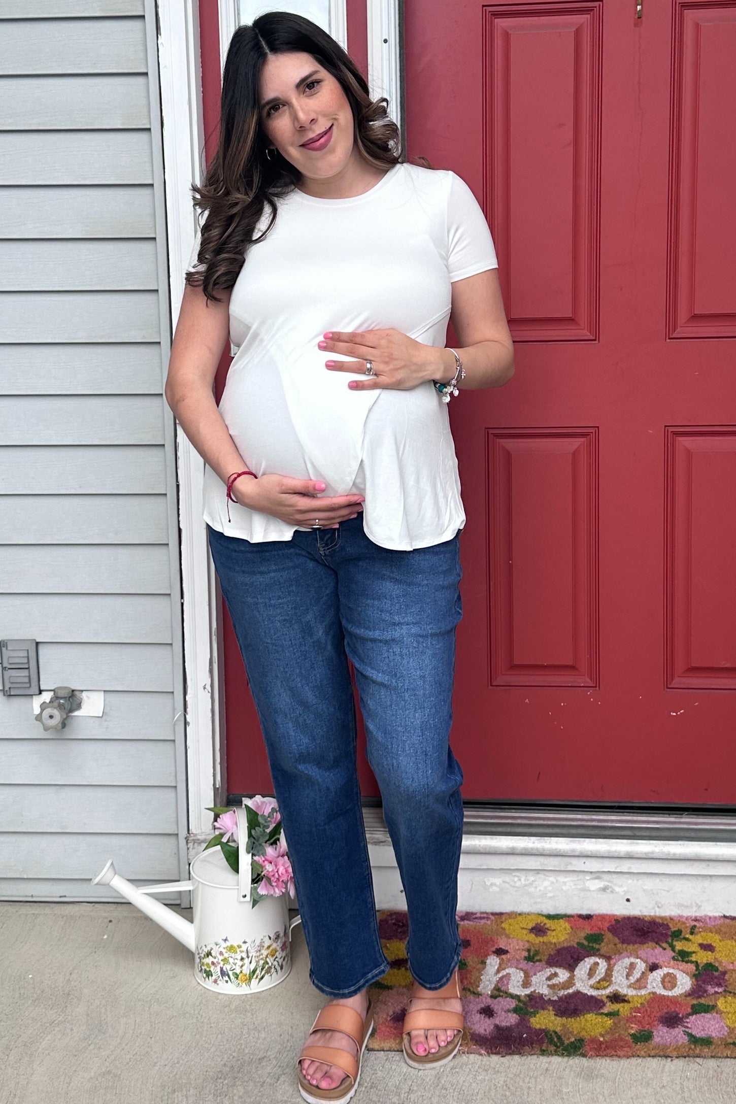 woman wearing a white maternity top and holding her baby bump, paired with blue jeans and sandals