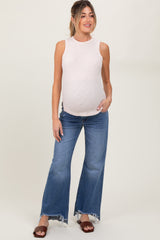 woman wearing a light pink sleeveless maternity top and blue flared jeans, showing her baby bump