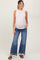 woman wearing a light pink sleeveless maternity top and blue flared jeans, showing her baby bump
