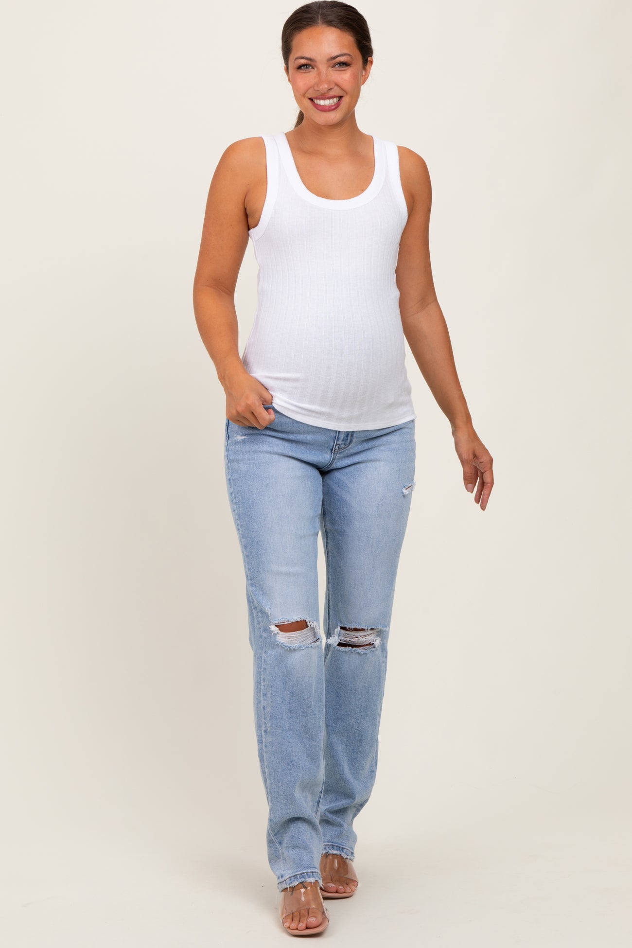 woman wearing a white ribbed maternity tank top and light blue distressed maternity jeans with a visible baby bump