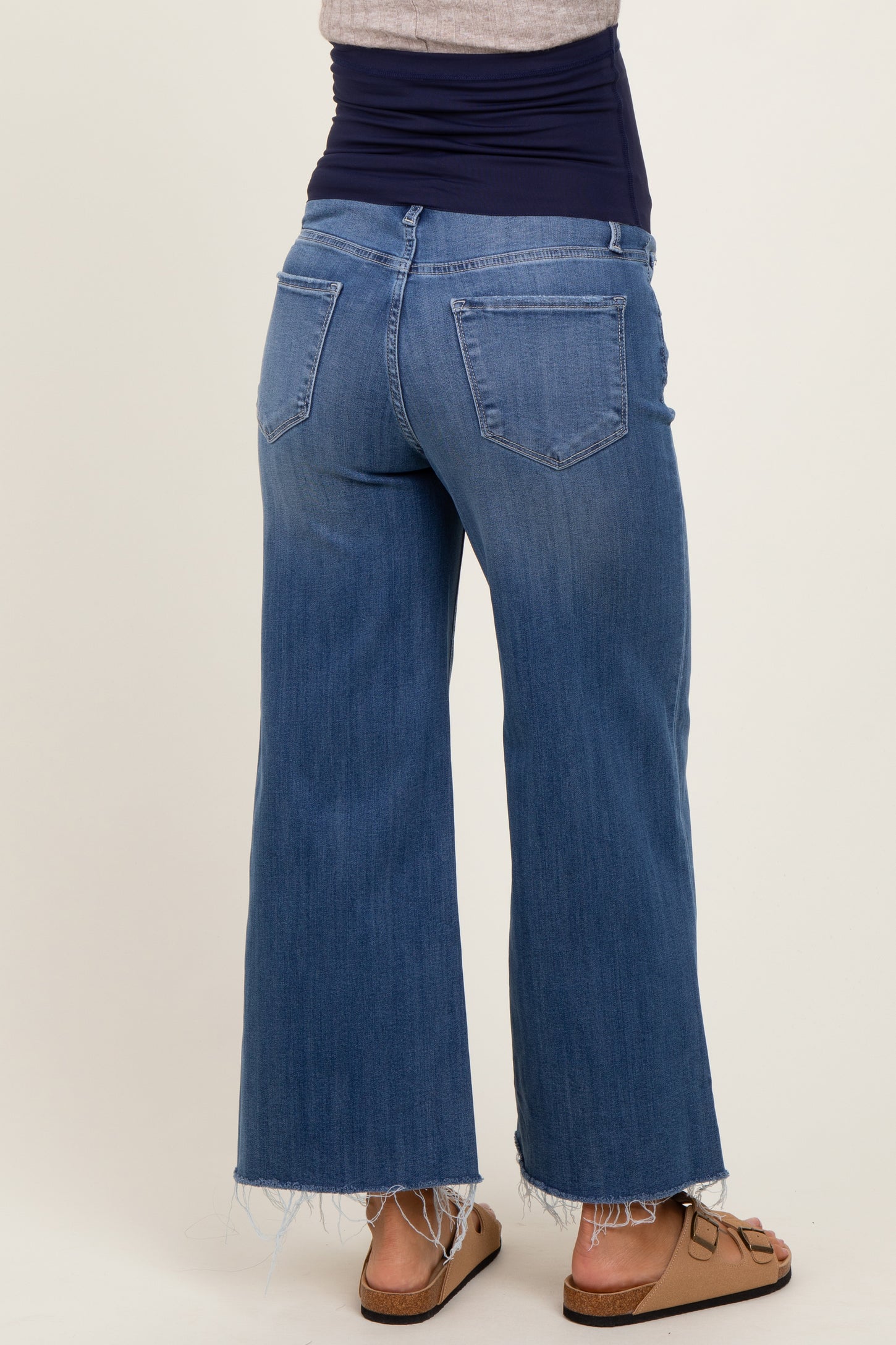 woman wearing a navy blue maternity top and light blue wide-leg maternity jeans, showing a baby bump from the back