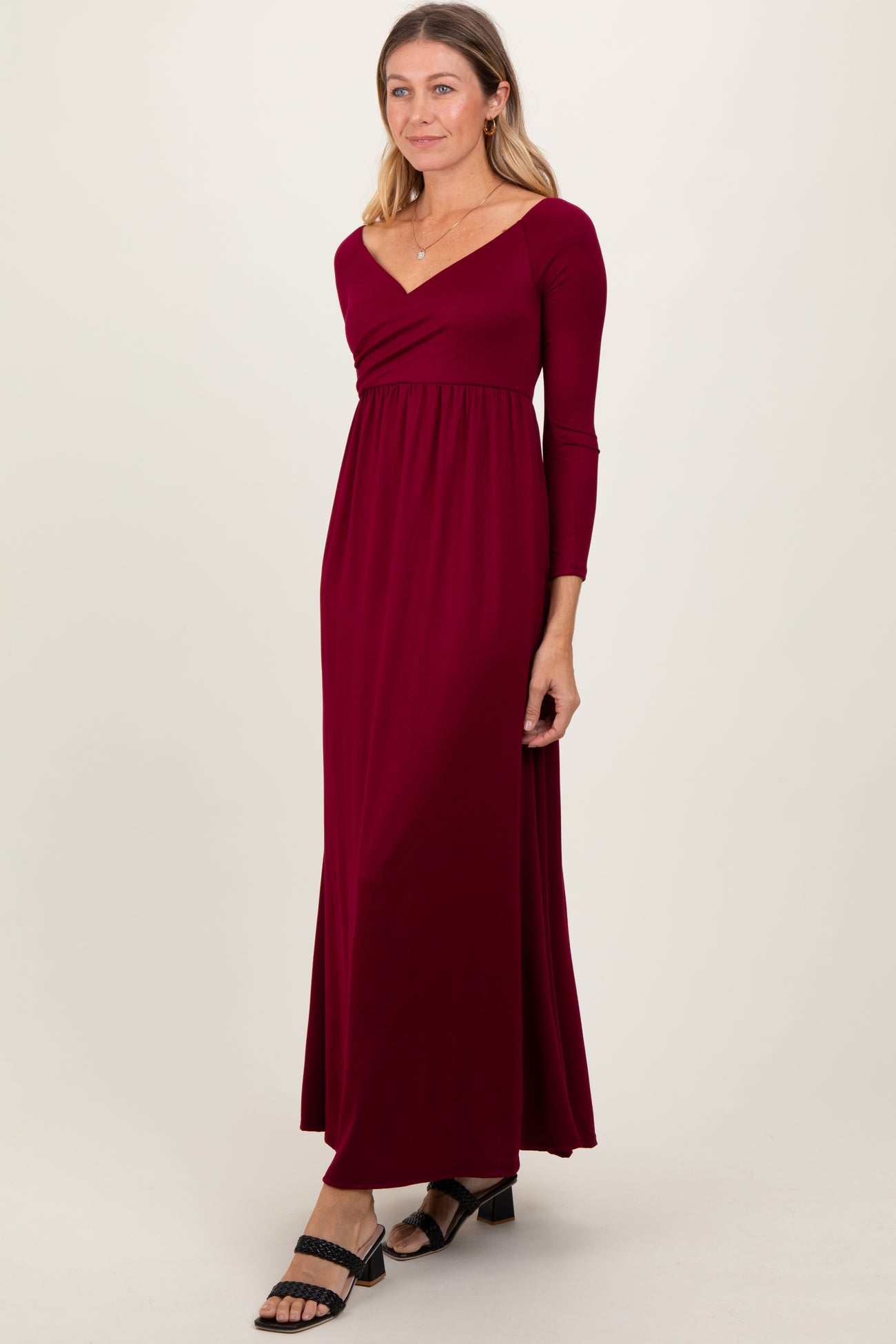 woman wearing a burgundy long sleeve maxi dress with a wrap front and fitted waist, styled with black sandals