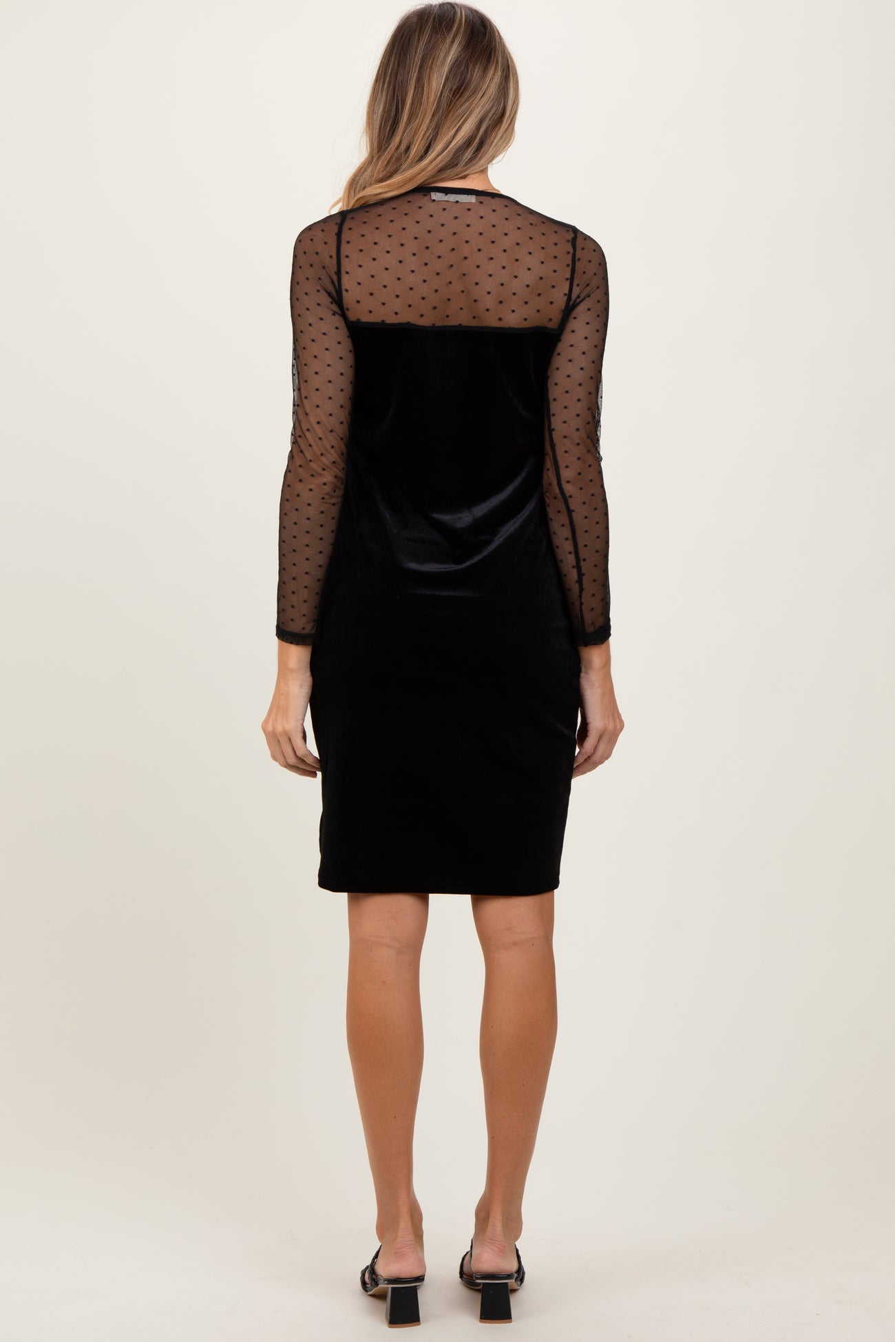 woman wearing a black velvet dress with long sheer polka dot sleeves, shown from the back