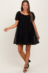 woman wearing a black maternity dress with a textured rose design and puff sleeves, standing and smiling