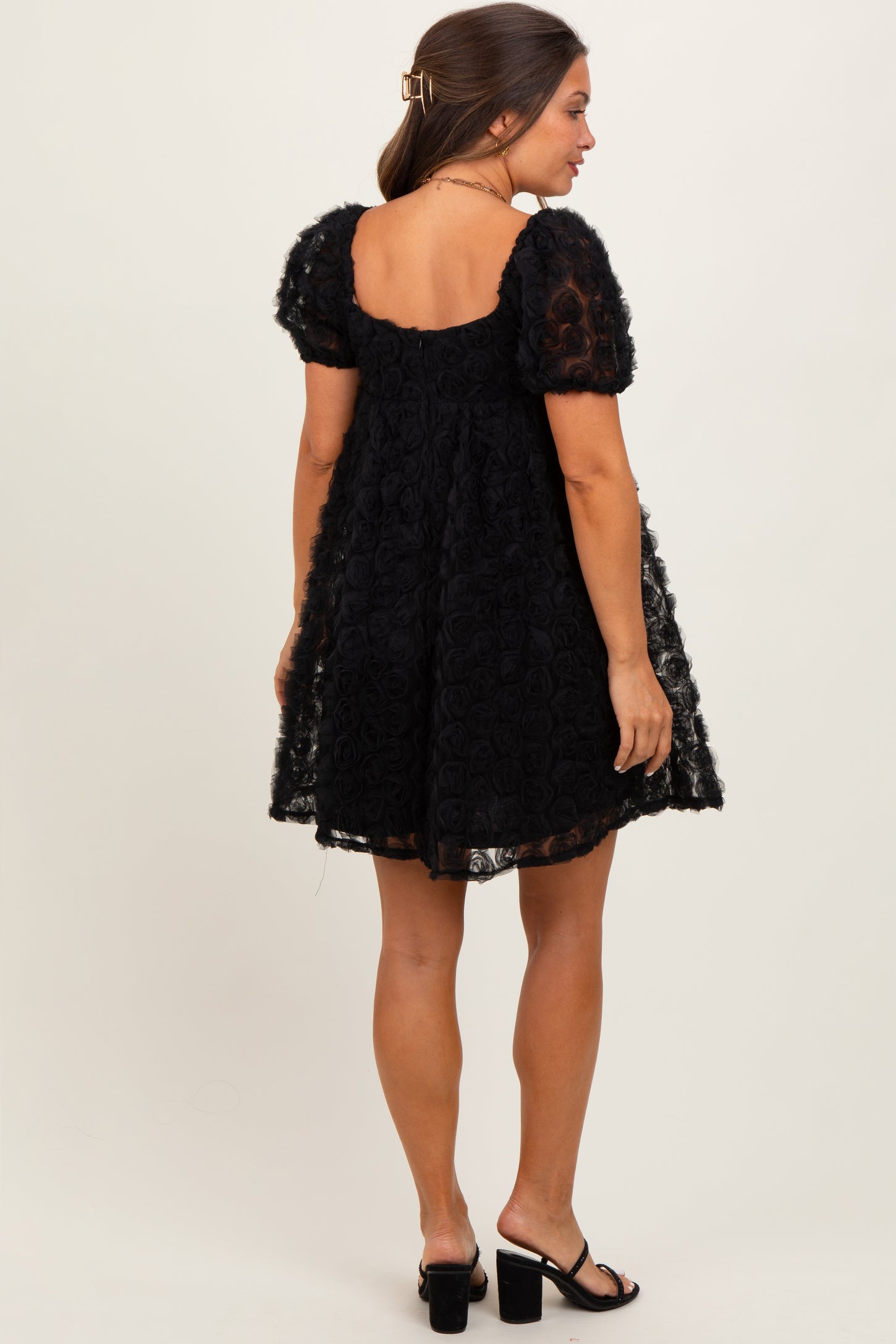 woman wearing a black maternity dress with short puff sleeves and a floral design, showing her back
