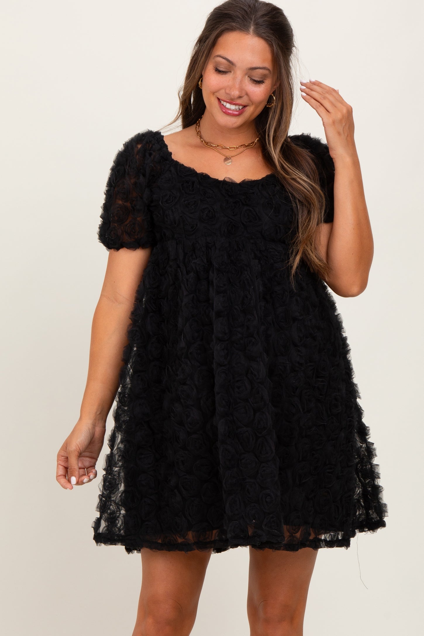 woman wearing a black maternity dress with a rose texture and short sleeves, smiling and posing with one hand in her hair