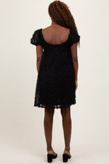 woman wearing a black short sleeve dress with floral lace detailing and a scoop back, standing with her back facing the camera