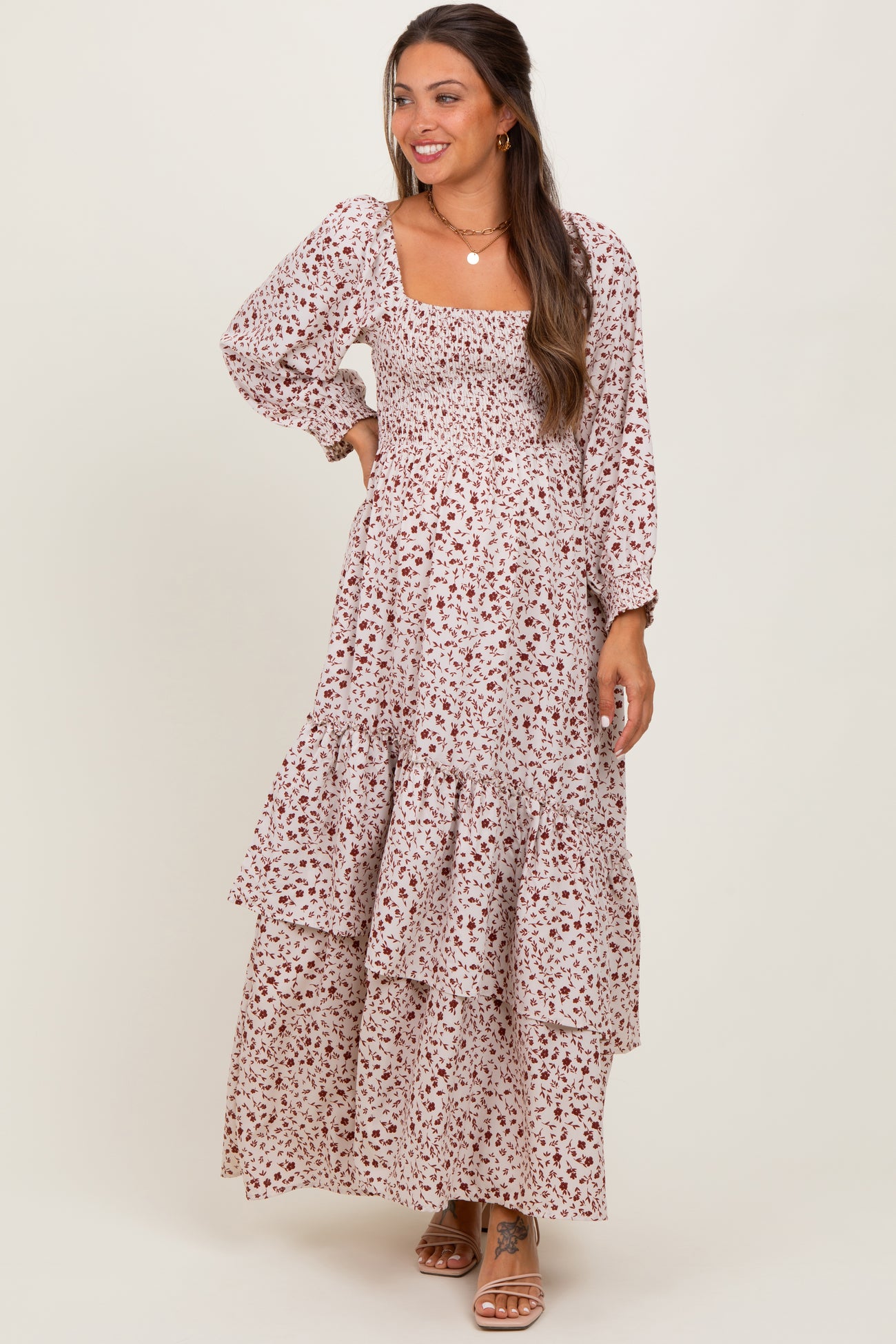 woman wearing a floral print maternity maxi dress with long sleeves and tiered ruffles, smiling while showing off her baby bump