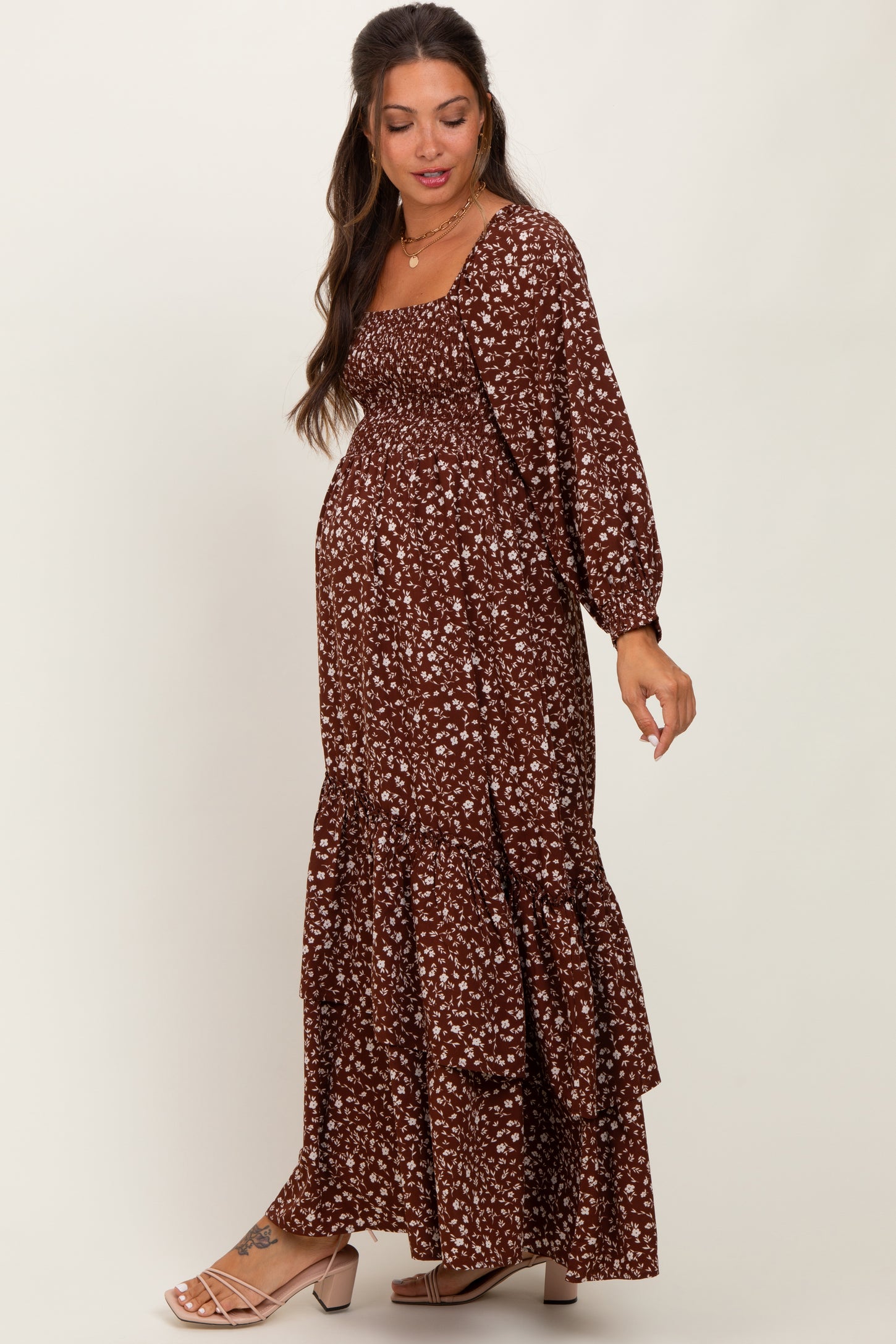 woman wearing a brown floral maternity maxi dress with long sleeves and ruffle details, showing her baby bump