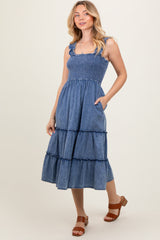 woman wearing a denim smocked midi dress with ruffled tiers and pockets, standing on a neutral background