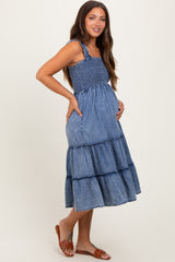 woman wearing a blue denim maternity maxi dress with smocked bodice and tiered skirt, holding her baby bump