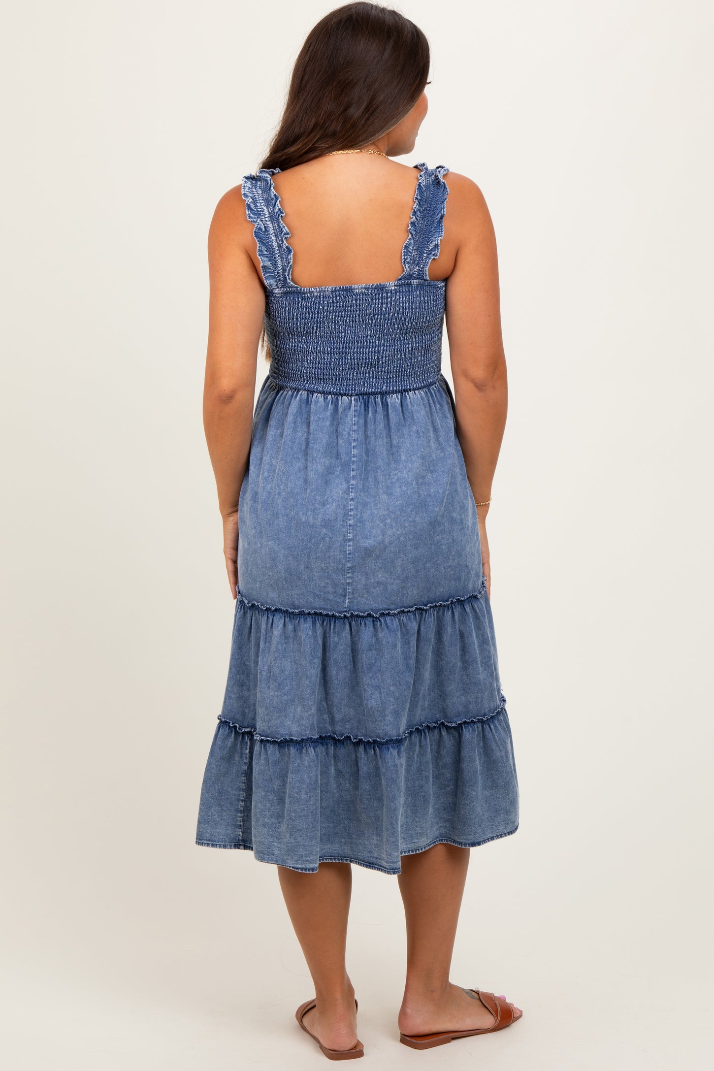 woman wearing a blue denim maternity dress with a smocked bodice and tiered skirt, showing her back